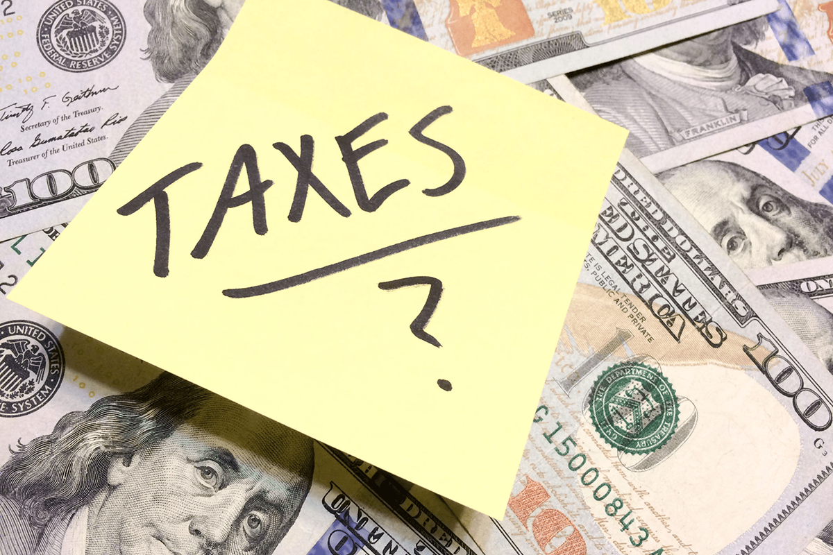 Sticky note with 'TAXES?' on US dollar bills.